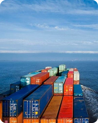 A cargo ship loaded with colorful shipping containers sails across a calm sea under a clear sky.